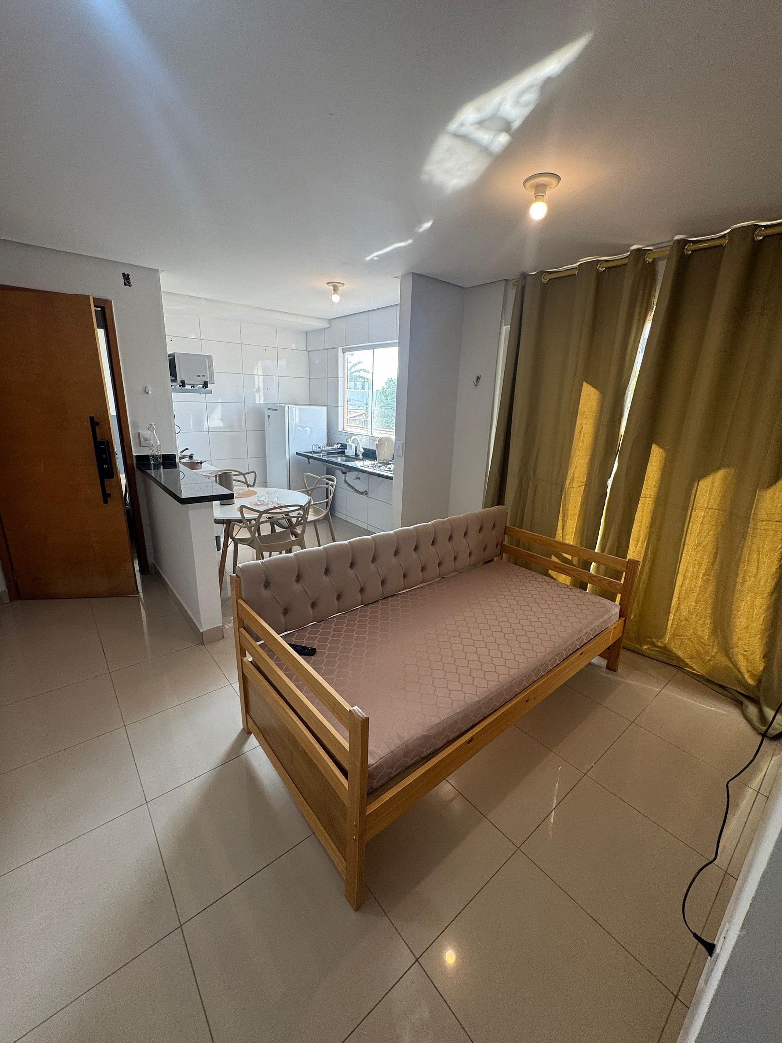 A compact room with a bed, a small kitchenette, a dining area, and a window with curtains.