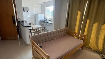 A compact room with a bed, a small kitchenette, a dining area, and a window with curtains.
