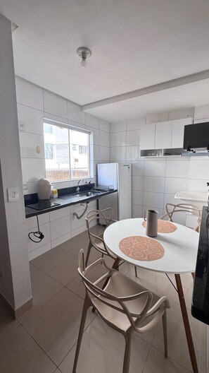 Une cuisine moderne avec des meubles blancs, une table de salle à manger ronde entourée de chaises et une fenêtre laissant entrer la lumière naturelle.