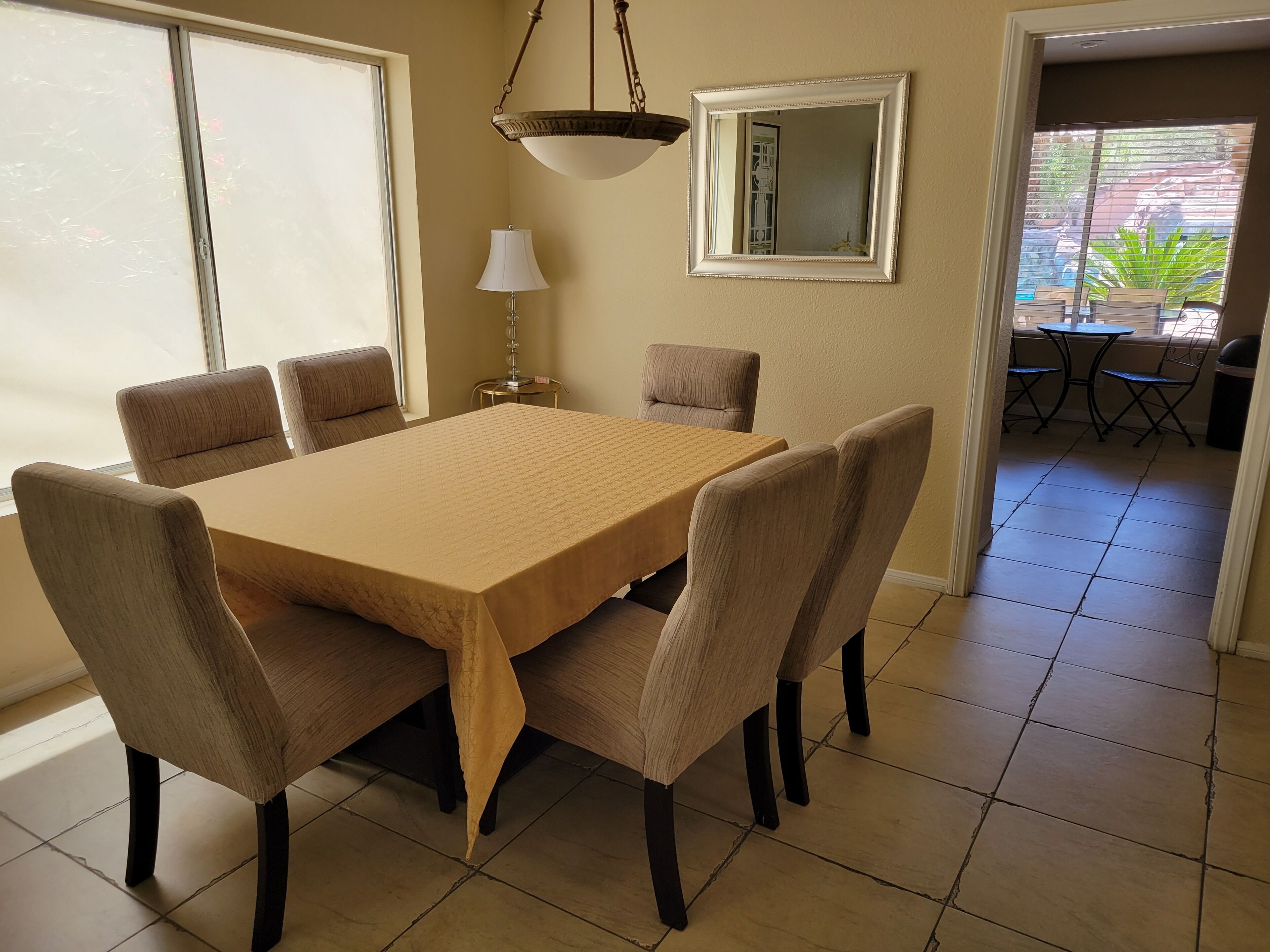 A dining area with a rectangular table, six chairs, a hanging light fixture, a lamp, and a mirror on the wall.