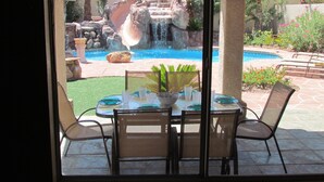 A dining area with a view of a backyard pool and waterfall. - Little Paradise in Las Vegas with Pool (Las Vegas)