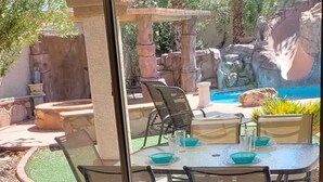 An outdoor patio with a table and chairs, a pool, and a waterfall. - Little Paradise in Las Vegas with Pool (Las Vegas)