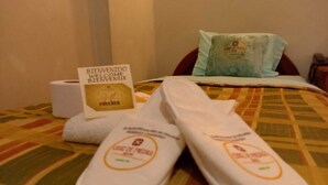 A bed with a patterned bedspread, a welcome sign, a pair of slippers, and a pillow with a logo.
