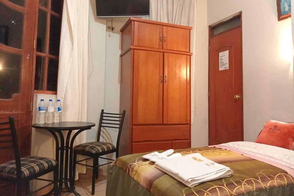 Une chambre d’hôtel comprenant un lit, une armoire en bois, un téléviseur, une petite table avec des chaises et une porte avec une pancarte.