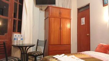 Habitación de hotel con cama, armario de madera, televisor, una mesita con sillas y una puerta con letrero.