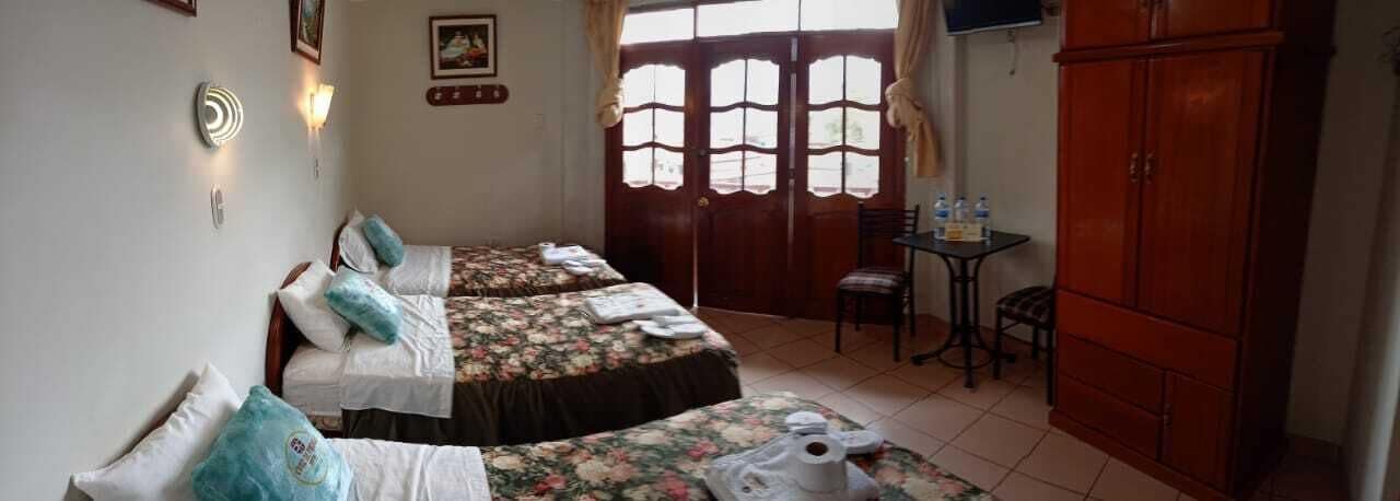 A room with two beds, a small table with water bottles, and a cabinet.