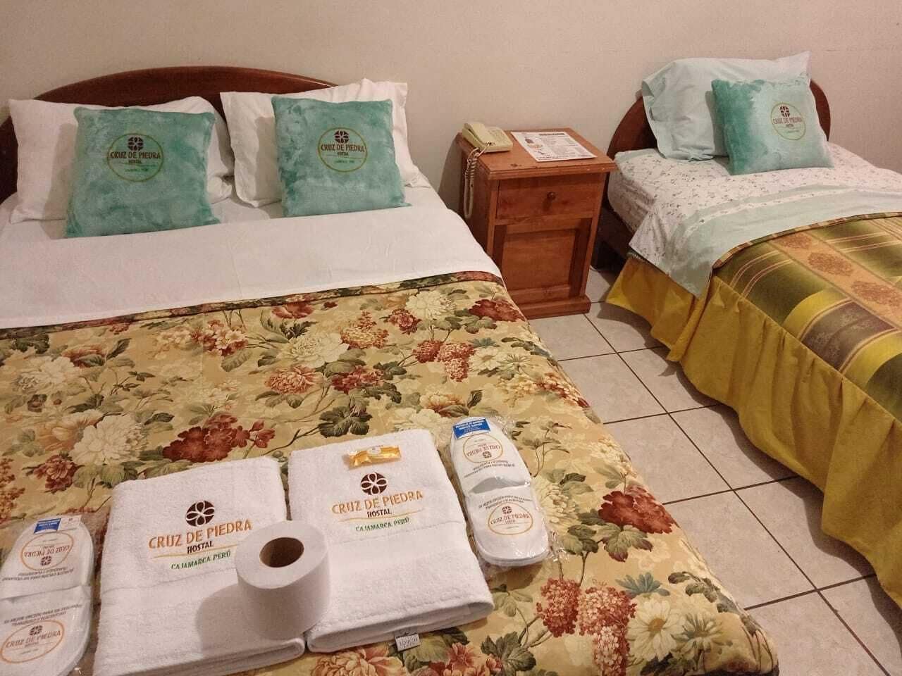 A hotel room with two beds, floral bedspreads, and towels with the hotel's logo.