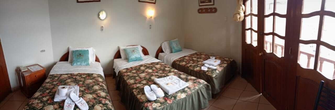 Quarto com duas camas, cada uma com colchas e toalhas estampadas com flores. Há luminárias na parede e uma porta de madeira com painéis de vidro.
