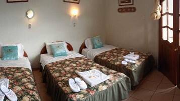 Quarto com duas camas, cada uma com colchas e toalhas estampadas com flores. Há luminárias na parede e uma porta de madeira com painéis de vidro.