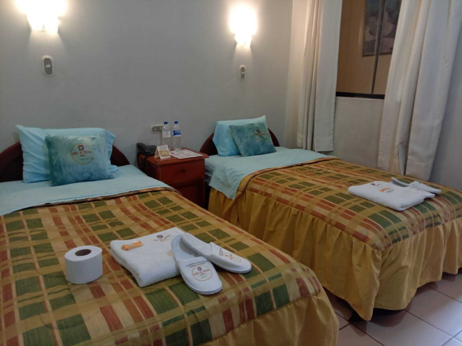 A hotel room with two beds, each with a patterned bedspread, pillows, and a nightstand with toiletries.