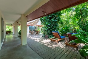 Área externa coberta com deck de madeira, cadeiras de lounge e plantas em vasos.