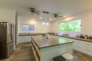 A modern kitchen with a central island, stainless steel appliances, pendant lighting, and a large window providing natural light.
