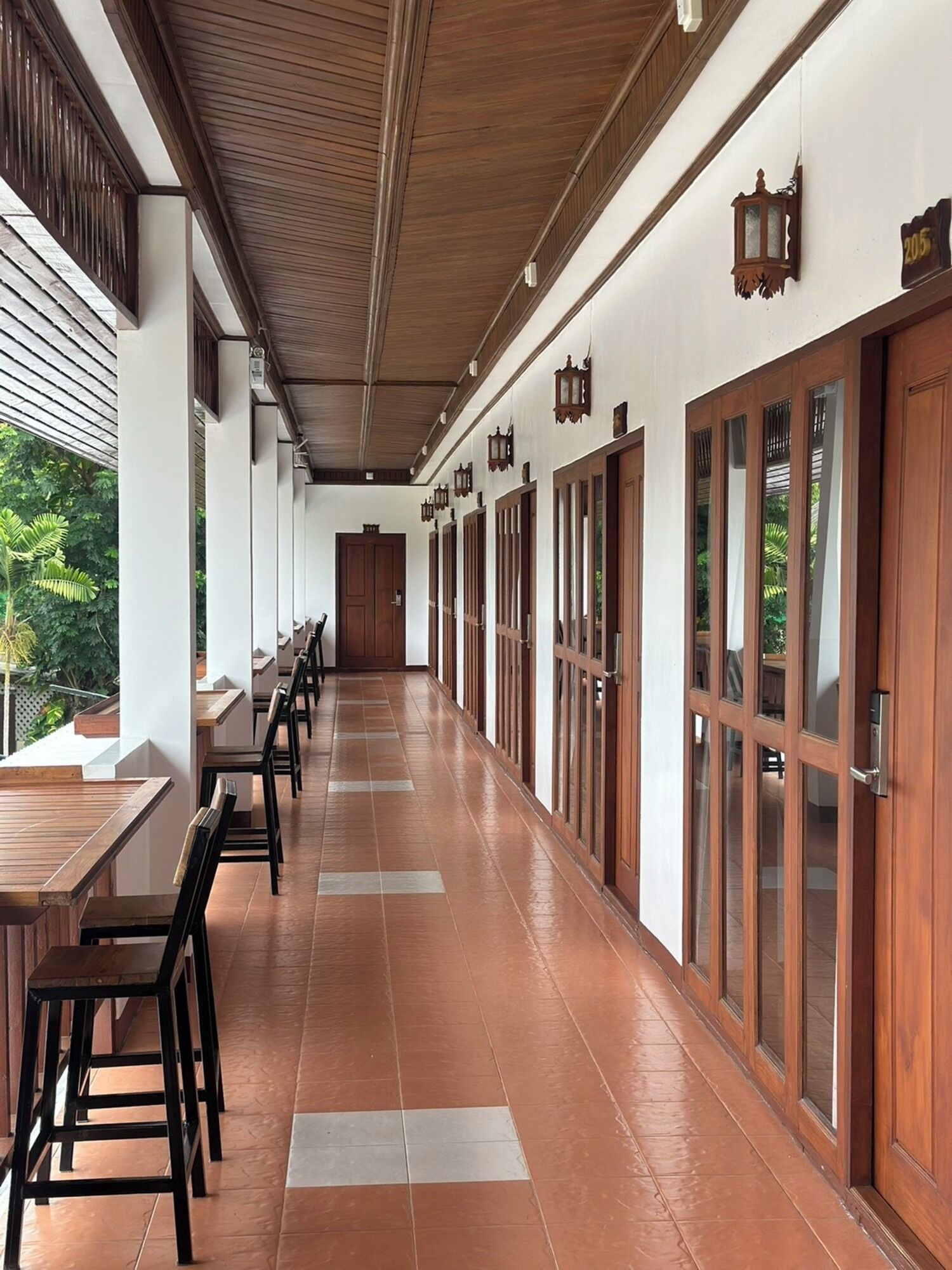 A corridor with wooden tables and chairs, a tiled floor, and wooden doors with glass panels.