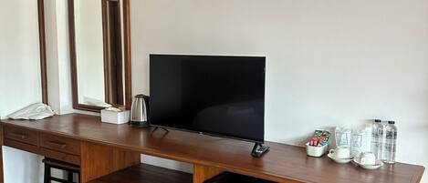 Un escritorio de madera con un televisor, un refrigerador pequeño, un espejo y algunos artículos de tocador.