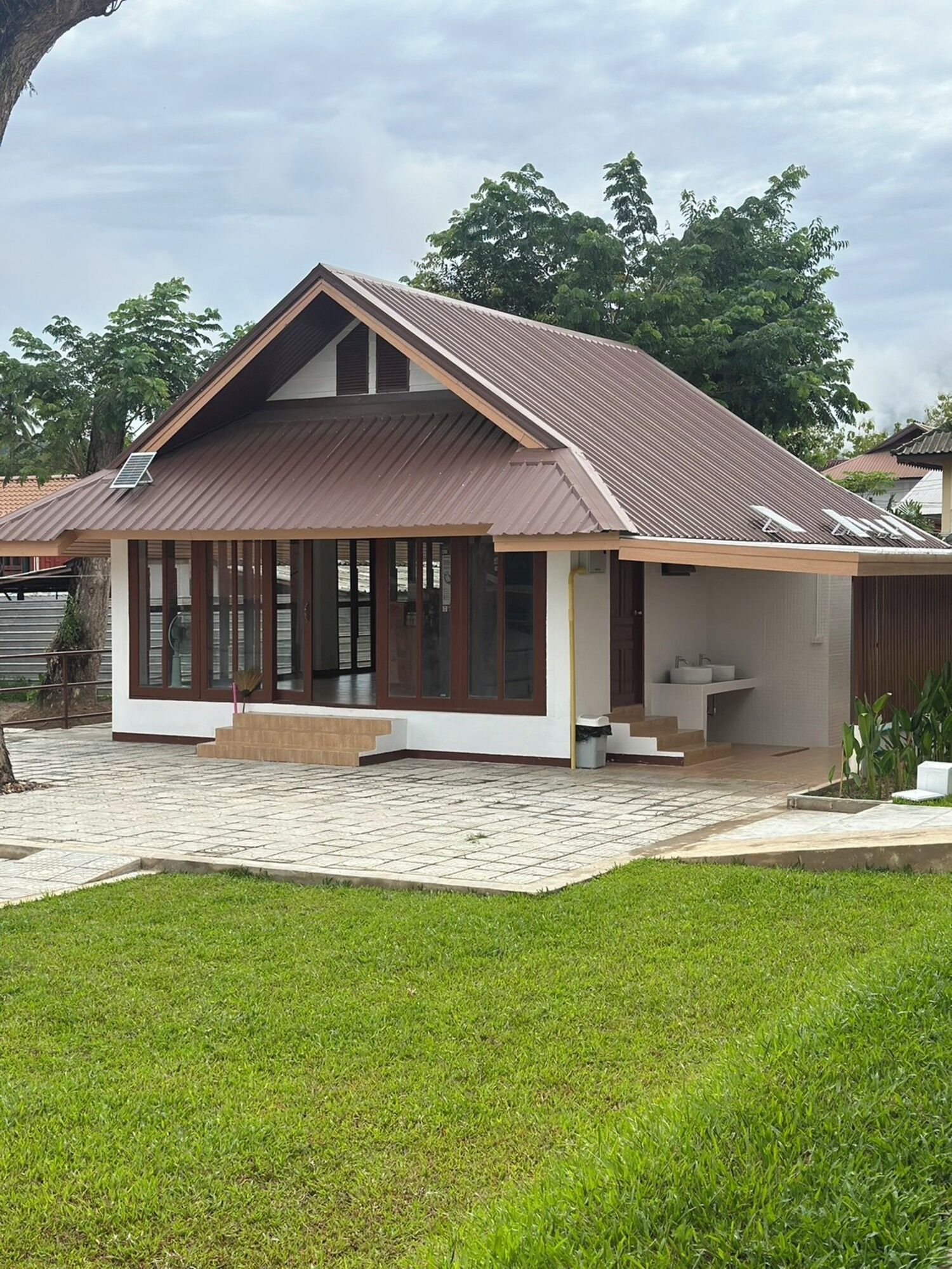A modern house with a sloped roof, large windows, and a paved patio.