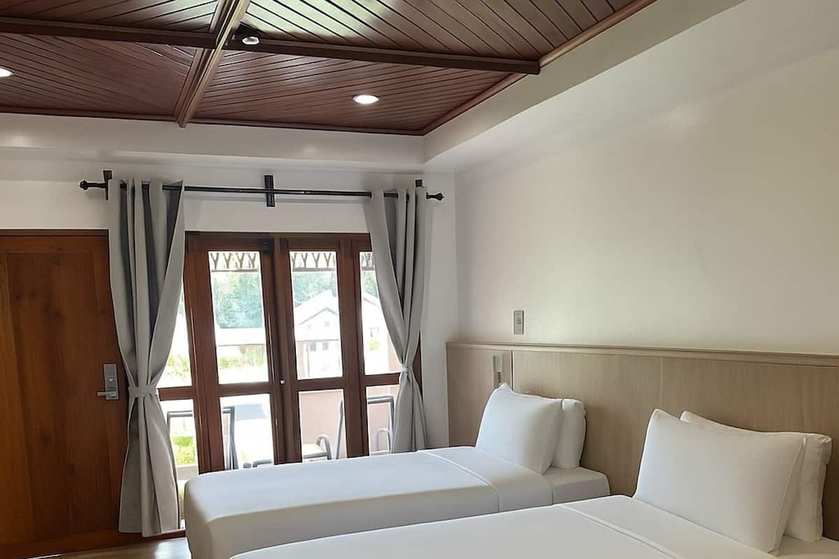 Een hotelkamer met twee bedden, houten vloer, houten plafond en uitzicht door een deur.