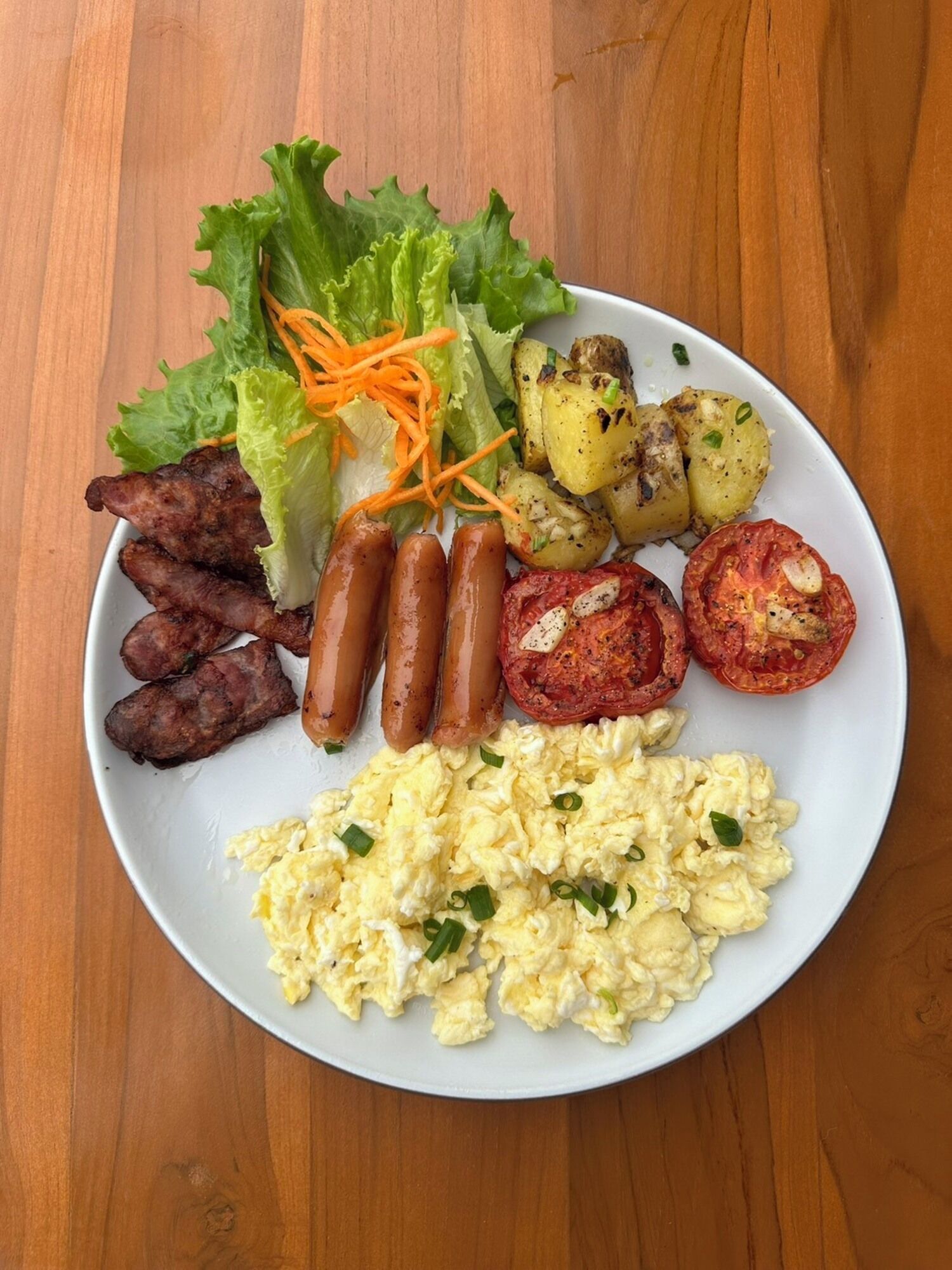 A plate of food including sausages, scrambled eggs, roasted potatoes, grilled tomatoes, and a side salad.