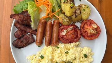 A plate of food including sausages, scrambled eggs, roasted potatoes, grilled tomatoes, and a side salad.