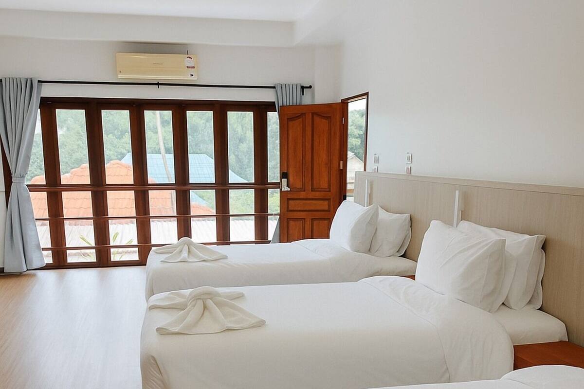 Een hotelkamer met twee bedden, een houten vloer, een groot raam met gordijnen en een airconditioner.