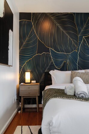 Un dormitorio con cama, mesita de noche y una pared con diseño de hojas.