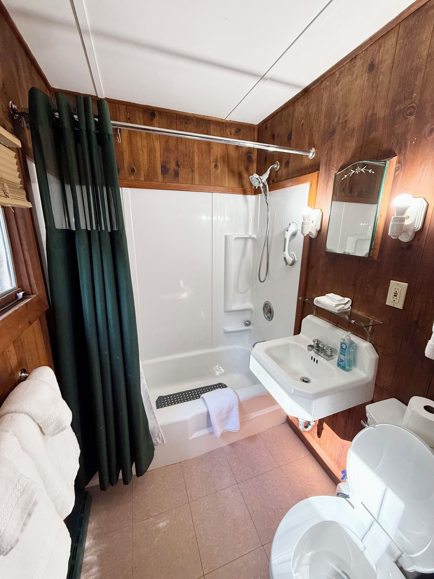 A bathroom with a shower, sink, toilet, and a mirror.