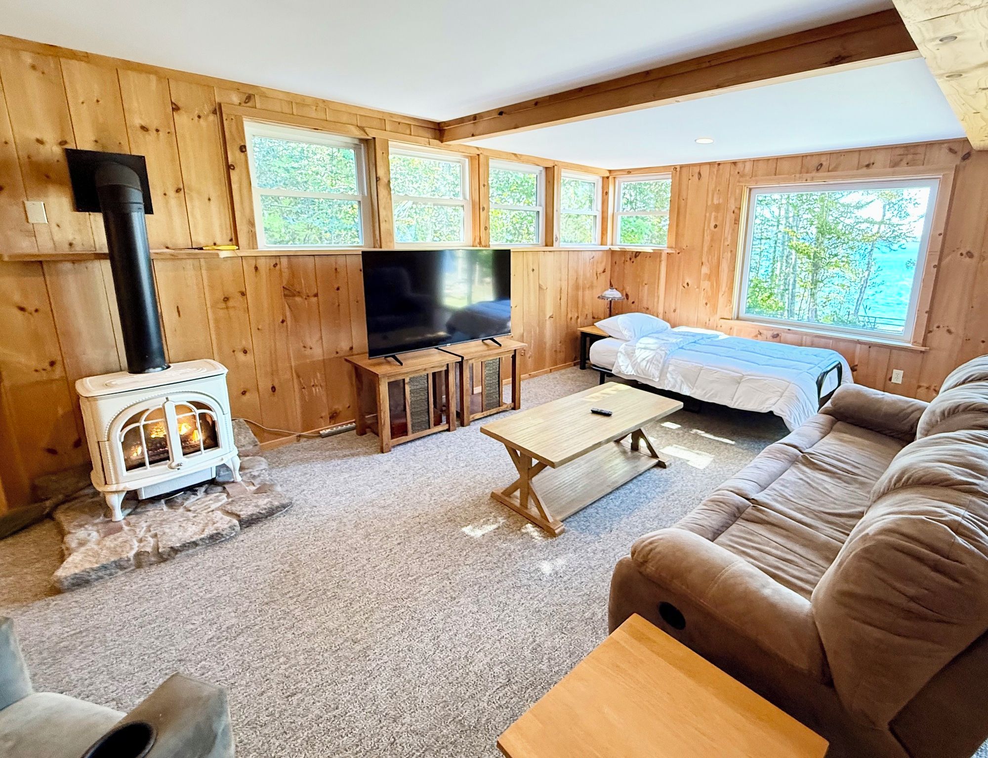 A cozy cabin interior with a wooden interior, a fireplace, a television, a sofa, and a bed.