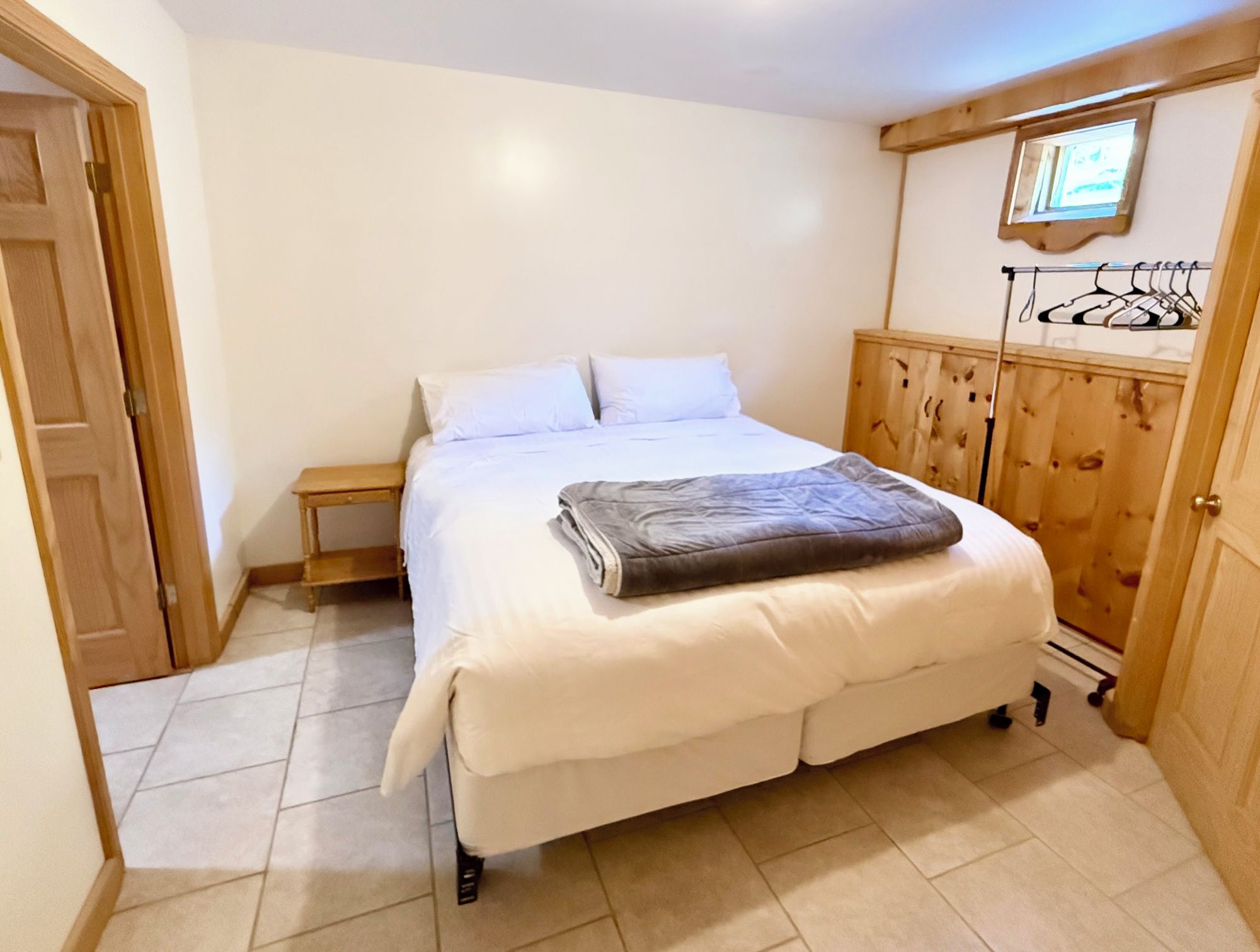 A bedroom with a bed, a wooden wardrobe, a small bedside table, and a door.