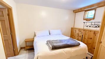 A bedroom with a bed, a wooden wardrobe, a small bedside table, and a door.