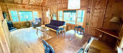 Interior de una cabaña de madera con una mesa de comedor, sillas, un sofá y un ventilador de techo.