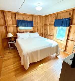 A room with a bed, a nightstand, a lamp, and a window with curtains.