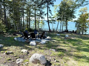 A lakeside camping area with Adirondack chairs and a fire pit.