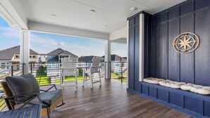 A covered outdoor area with wooden flooring, seating, and a decorative wall.