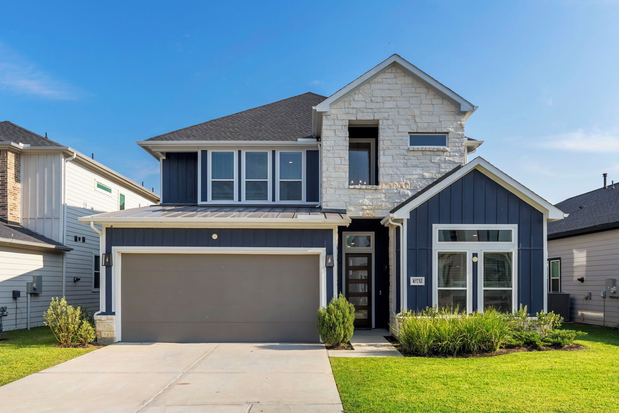 A two-story house with a garage, a stone facade, and a well-maintained lawn.