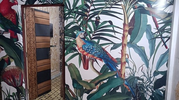 A room with a patterned floor, a door with a geometric design, and a wall mural featuring a parrot and tropical plants. - Shri Premanand Ji Niwas Sthan (Vrindavan)