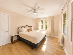 A bedroom with a bed, a nightstand, a ceiling fan, and a window with curtains.