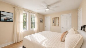 A bedroom with a bed, a ceiling fan, two windows with curtains, a door, and a wall-mounted mirror. - Hill Top Pet-Friendly Cabin w/Hot Tub / Fire Pit (Pigeon Forge)