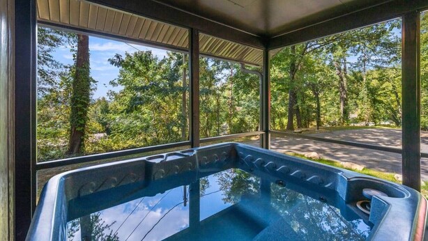 A hot tub in a covered outdoor area with large windows offering a view of a road and trees.