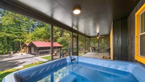 A hot tub on a covered porch with a view of a red-roofed building and trees.