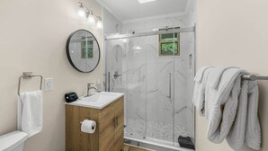 A modern bathroom with a glass-enclosed shower, a wooden vanity, a round mirror, and a towel rack.