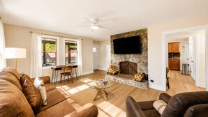A living room with a fireplace, a dining area, and a kitchen visible through an open door. - Hill Top Pet-Friendly Cabin w/Hot Tub / Fire Pit (Pigeon Forge)