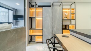 Una camera d'hotel moderna con un letto grande, una TV fissata al muro, una scrivania con una sedia e scaffali a parete con vani illuminati.