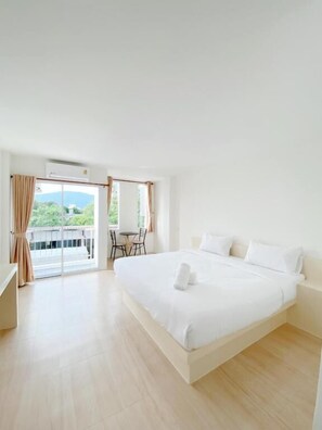 A spacious bedroom with a large bed, a small table with chairs, and a balcony with curtains. - Tanatnan Hotel (Ranong)