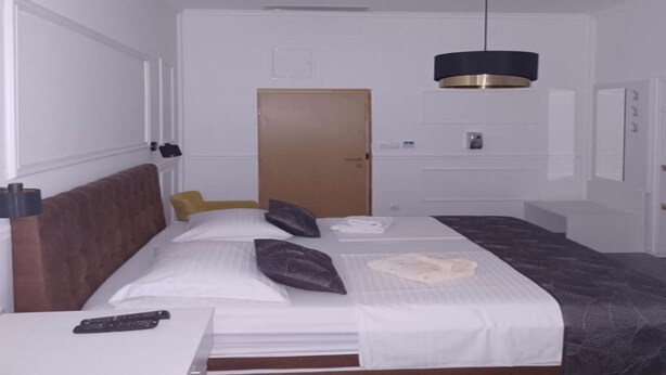 Habitación de hotel con cama, mesita de noche, control remoto, puerta y una lámpara colgante.