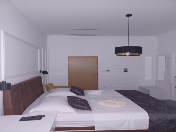 A hotel room with a bed, a bedside table, a remote control, a door, and a pendant light.
