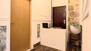 Un pasillo con una puerta de madera, un mostrador de recepción blanco, una pared de piedra y una planta en maceta.