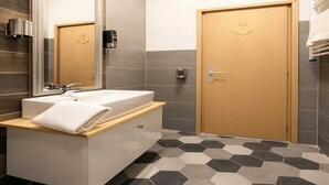 Un baño moderno con un espejo grande, un lavamanos blanco, una puerta de madera y suelo con diseño hexagonal.