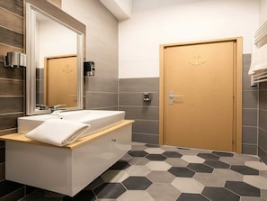 A modern bathroom with a large mirror, a white sink, a wooden door, and hexagonal patterned flooring.