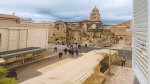Un edificio histórico con un campanario, una zona cubierta con gente y una calle en primer plano.
