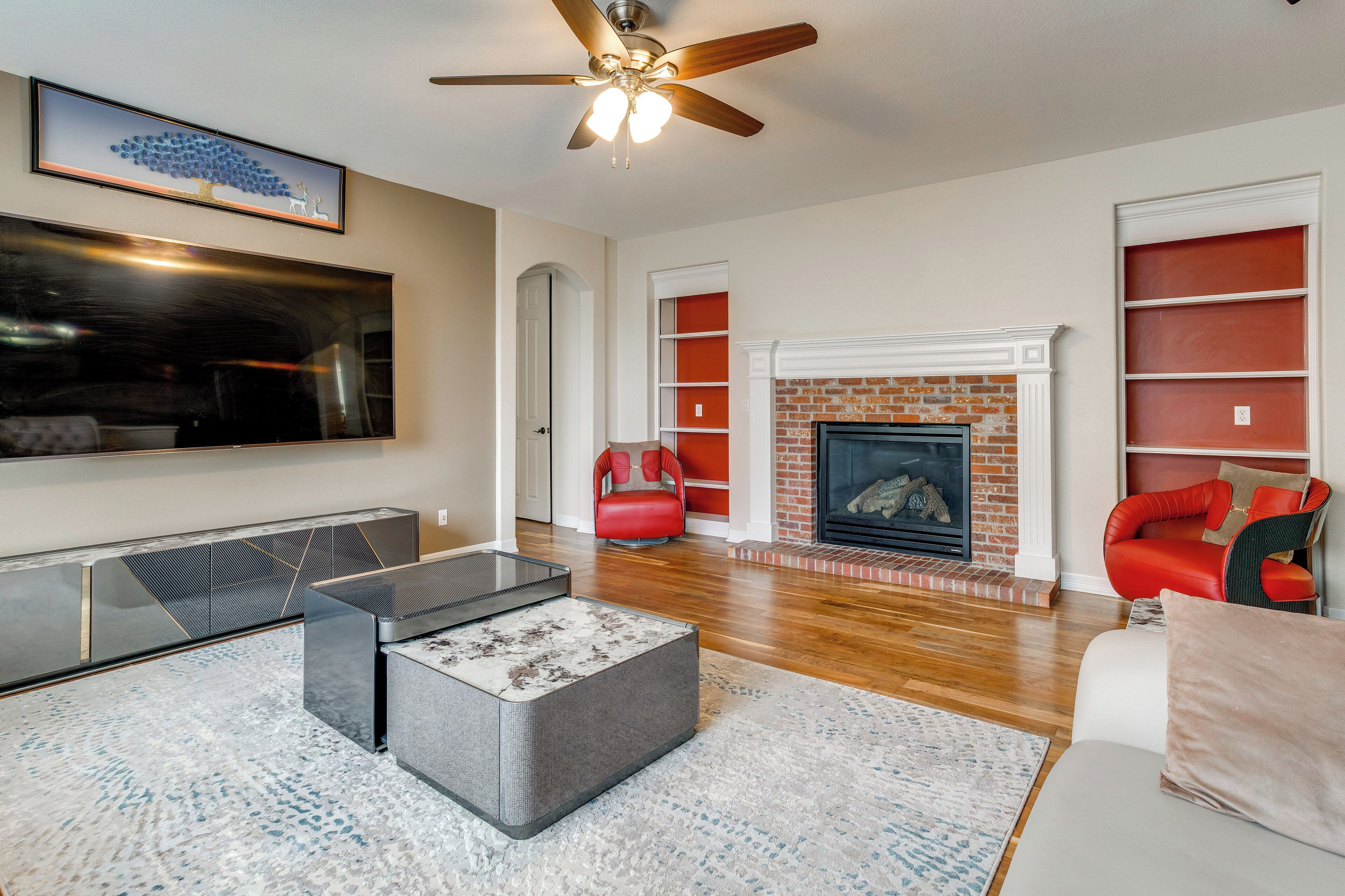 A modern living room with a fireplace, red and white furniture, and a flat-screen TV.