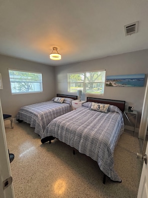 A bedroom with two beds, a ceiling light, a window with blinds, and a painting on the wall.
